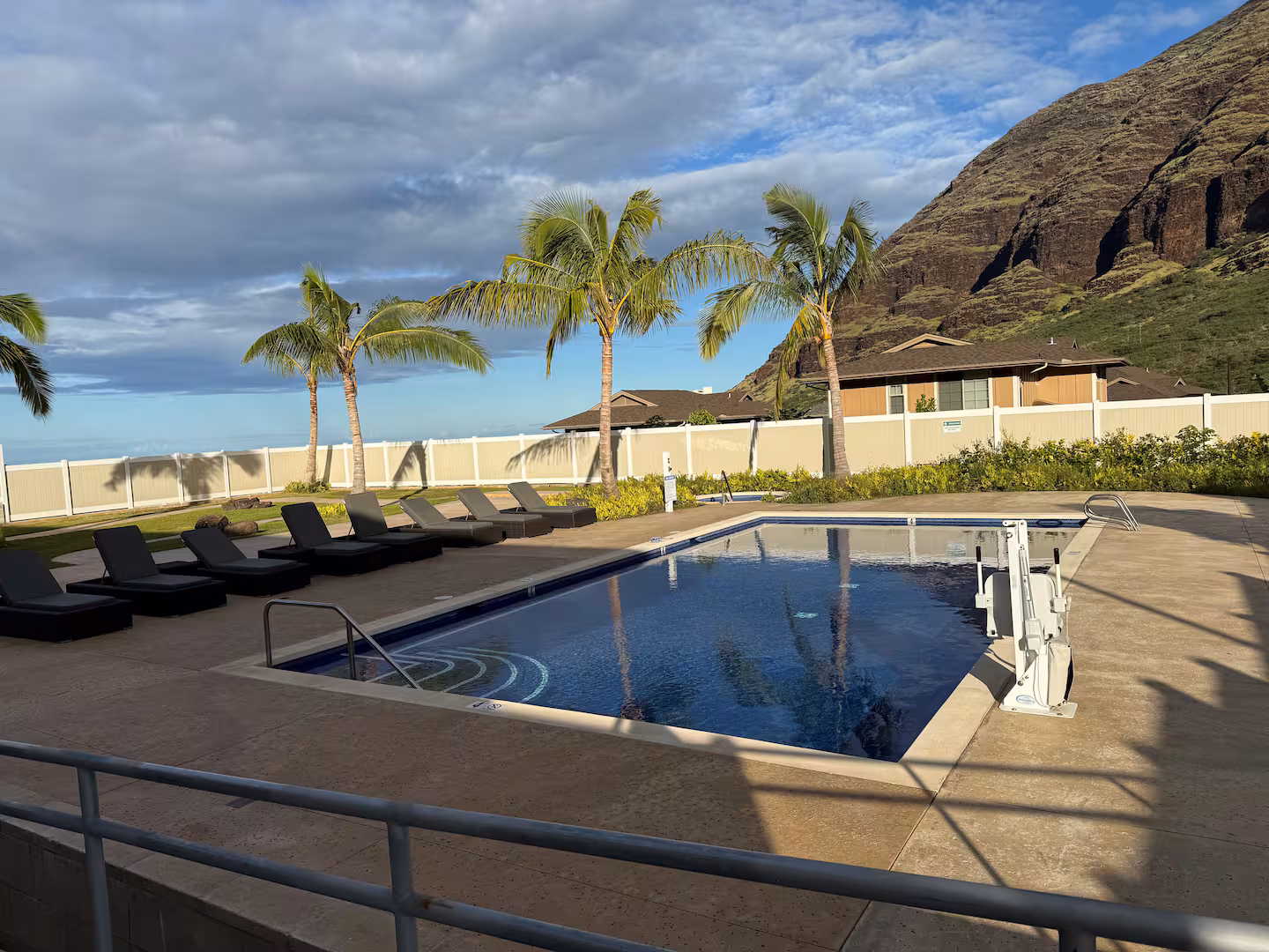 The community swimming pool lined with sun loungers, palm trees and the mountain ridge behind
