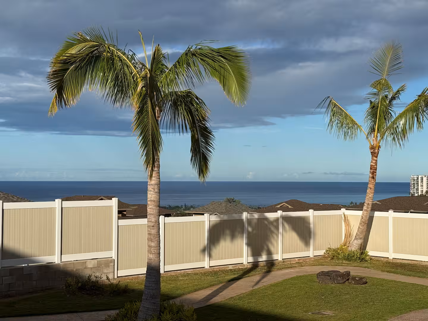 Ocean view from the garden over the fence line, framed by two palm trees
