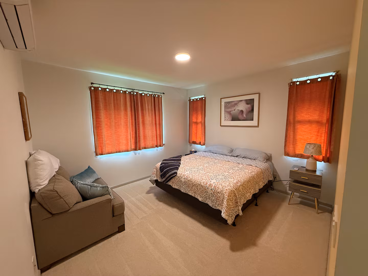 Master bedroom with a king bed, armchair and warm orange curtains