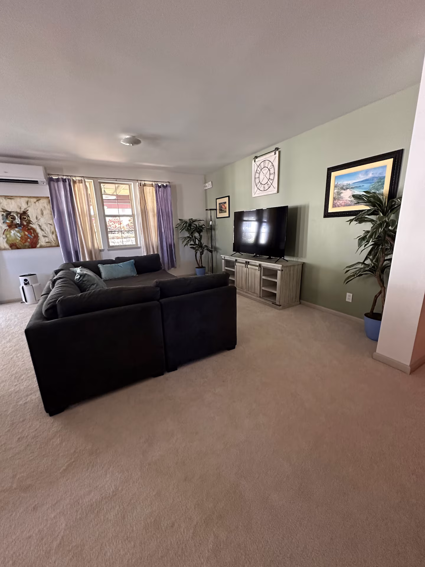 Living room with a large sectional sofa, wall-mounted TV and a sage green feature wall