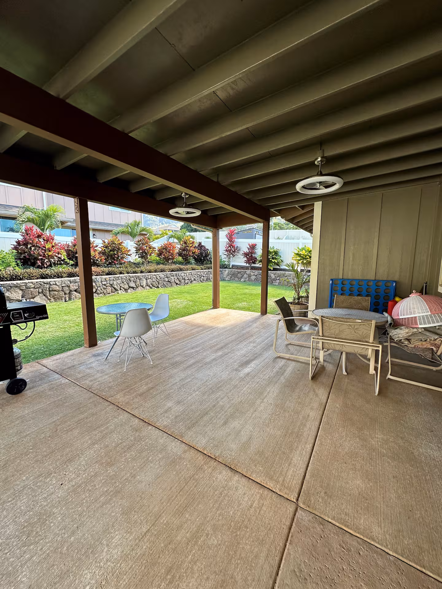 Covered lanai with patio furniture and a giant Connect Four set, opening onto the fenced lawn