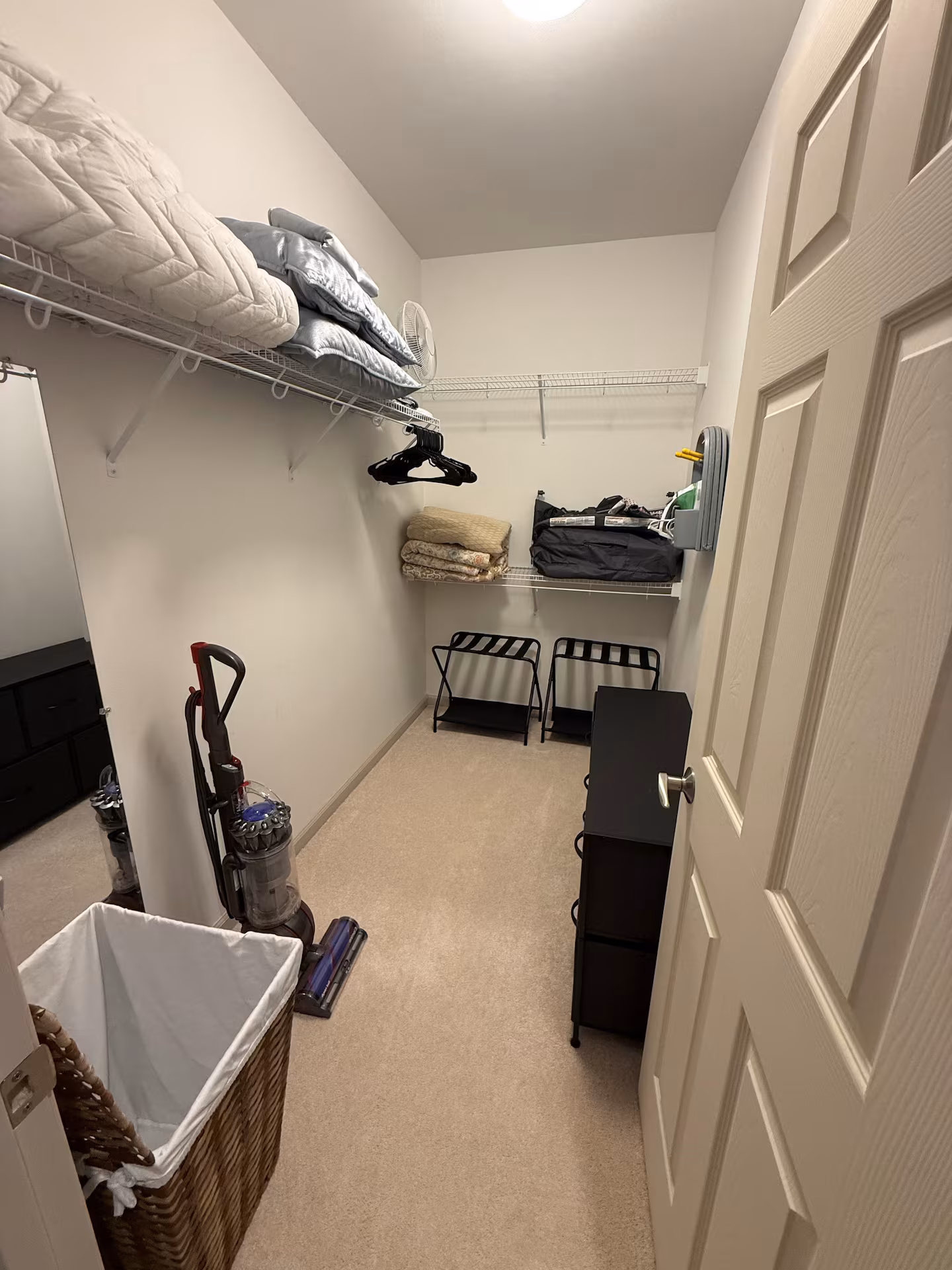 Walk-in closet with hanging space, luggage racks, spare bedding and a vacuum