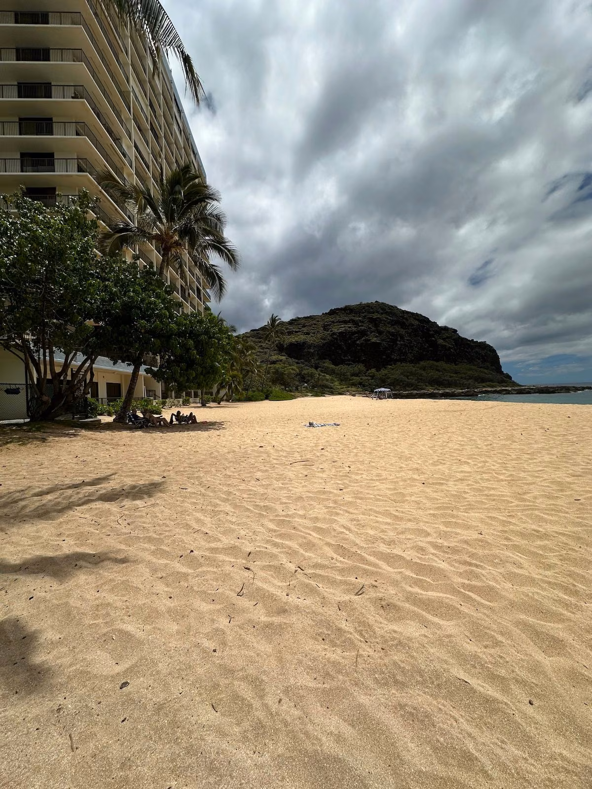 Wide empty sand at Papaoneone Beach with the Hawaiian Princess building and the rocky headland at the far end
