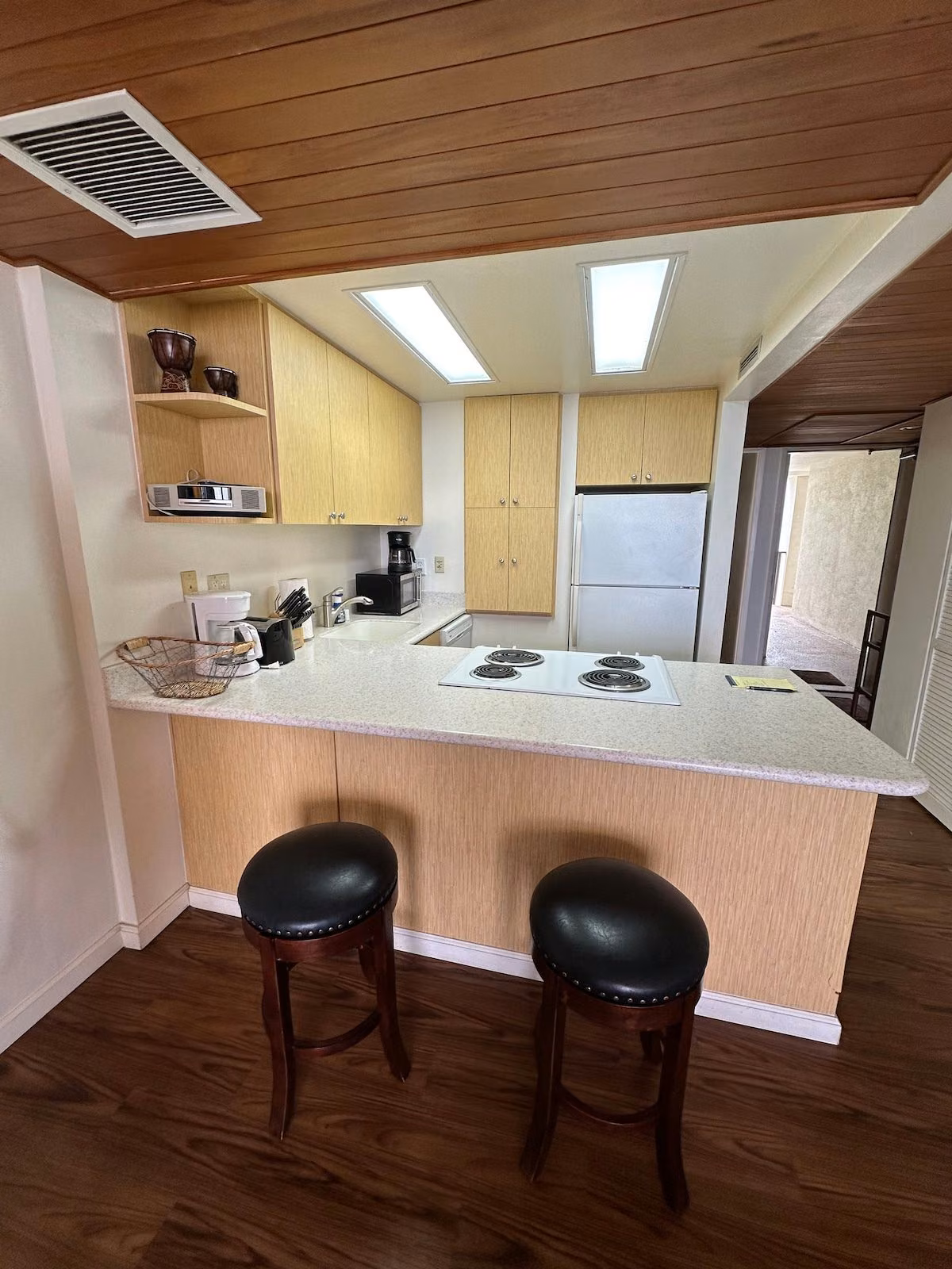 Galley kitchen with a light wood breakfast bar, two stools, cooktop and full-size fridge