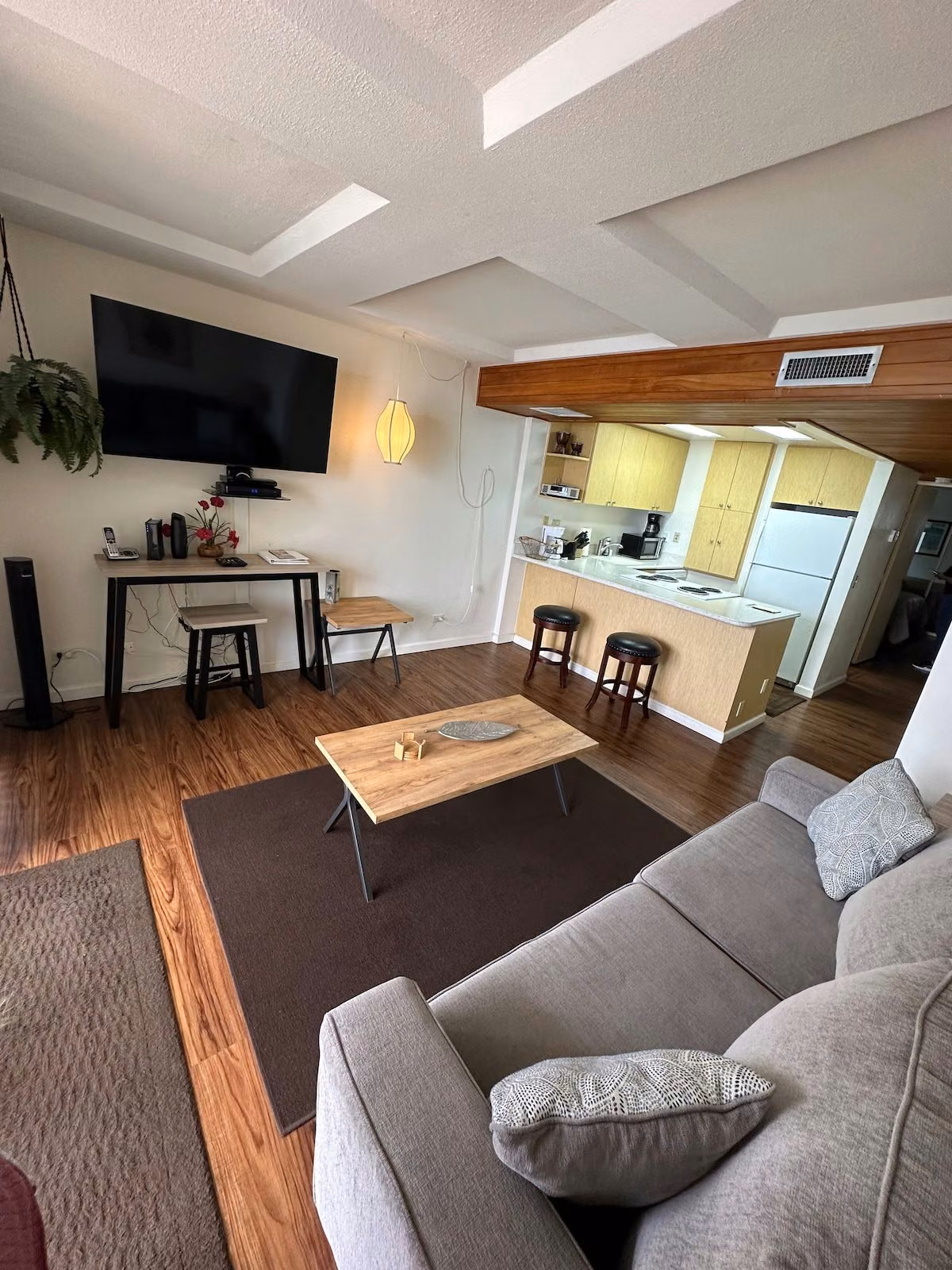 Living room with the TV, stereo and desk along one wall and the kitchen visible beyond
