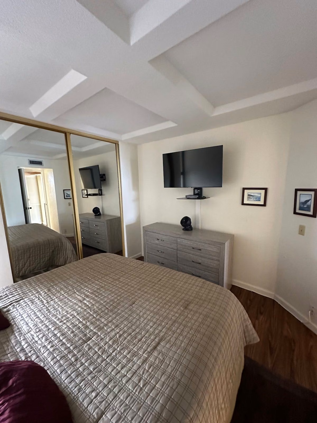 Second view of the bedroom with a wall-mounted TV, dresser and mirrored wardrobe