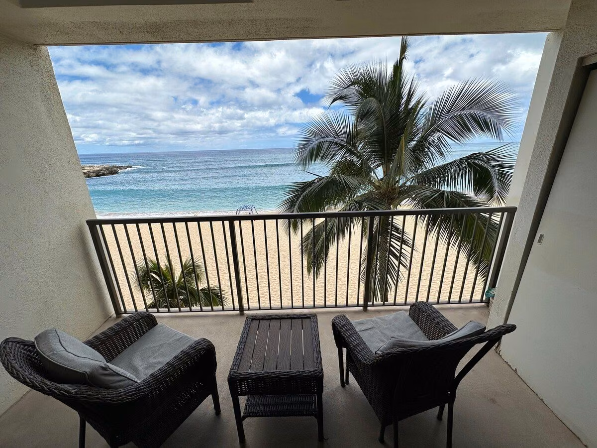 Private lanai with wicker chairs and a low table looking straight out over the beach and ocean