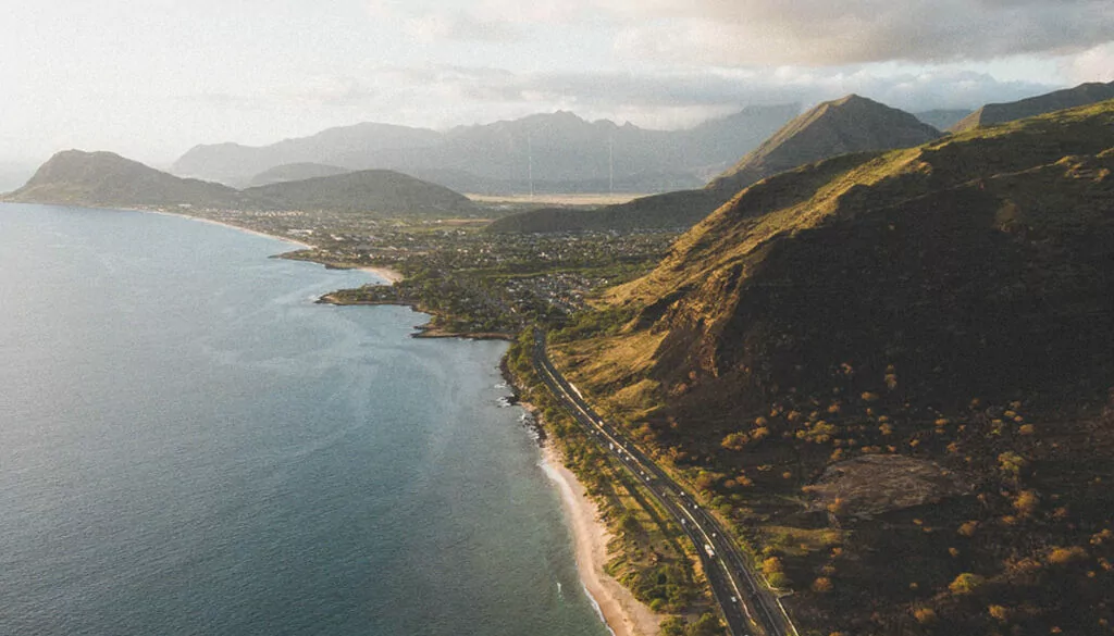 Aerial view of Oahu's west side coastline, with Farrington Highway running along the shore toward Waianae and the Waianae mountain range behind